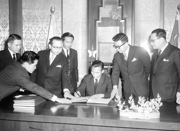박정희 대통령이 1965년 12월18일 청와대에서 정일권 총리(왼쪽에서 세 번째), 이동원 외무부장관(오른쪽에서 세 번째), 김동조 주일대사(오른쪽에서 두 번째) 등이 지켜보는 가운데 한일조약 제협정의 비준서에 서명하고 있다. 일본으로부터의 자금유입의 길이 열렸다. 사진= 국가기록원.
